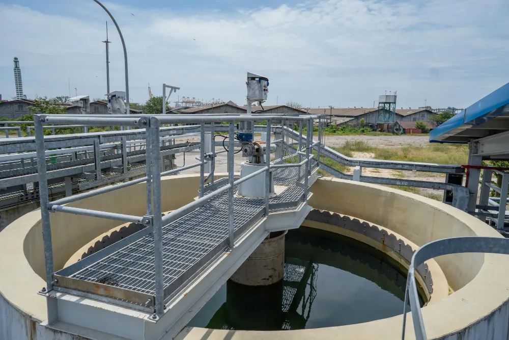 Estrutura industrial com canalização e tanque circular com água tratada, plataformas metálicas e equipamentos de dosagem visíveis em estação de tratamento, foco em processos de cloro gás vs hipoclorito