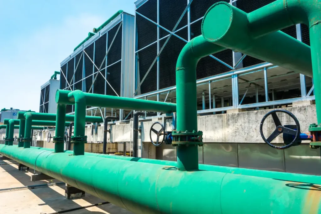 controle de odores em ete: Tubulação industrial verde e válvulas em uma estação de tratamento, com estrutura metálica e rodas de controle ao fundo, em ambiente externo